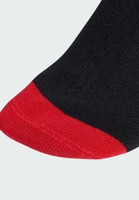 Černá ponožka s červeným špičkou a žebrovanou texturou. Červený akcent výrazně kontrastuje s černým materiálem. Pohled zblízka na oblast špičky.