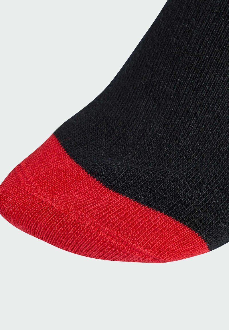 Svart strumpa med röd tå och ribbad textur. Den röda accenten står i stark kontrast mot det svarta materialet. Närbild på tåområdet.