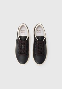 Sorte lær sneakers med en glat tekstur, rund tå og mørkebrune snørebånd. Har en hvid sål og prægede logo på siden.