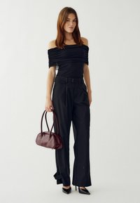 Čierny top s odhalenými ramenami a zhrnutou textúrou, skombinovaný s čiernymi nohavicami s vysokým pásom a malou bordovou kabelkou vyrobenou z hladkej kože.