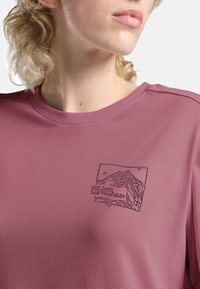 Chemise à manches courtes de couleur rose en tissu lisse ; présente un graphique de montagne noir et un logo sur la poitrine gauche.