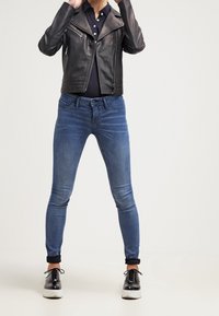 Black leather biker jacket, dark blue fitted jeans, and black and white lace-up shoes. Straight leg cut, zippered pockets, cuffed hems.