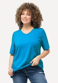 T-shirt turchese a V con maniche corte, realizzato in materiale morbido. Abbinato a jeans blu con dettagli strappati.
