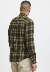 Camisa de cuadros verdes con patrones de cuadros marrones y blancos, puños abotonados y cuello puntiagudo, hecha de una tela suave y texturizada.