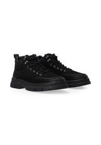 Schwarze High-Top-Schuhe aus Wildleder mit glatter Oberfläche, versehen mit Metallösen, runden Schnürsenkeln und einer dicken Gummisohle mit strukturierten Details.