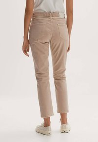 Jeans rectos de color beige claro con una cintura de altura media, bolsillos traseros y dobladillos ligeramente enrollados, combinados con zapatillas blancas. Textura suave.