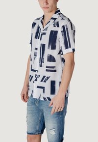 Korte mouwen button-up shirt in het wit met blauwe geometrische patronen. Gemaakt van lichtgewicht stof. Gecombineerd met lichtblauwe ripped denim shorts.
