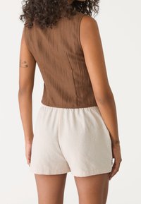 Brązowa, teksturowana bluzka bez rękawów z zaokrąglonym dekoltem w połączeniu z kremowymi, lekkimi szortami na elastycznej talii.