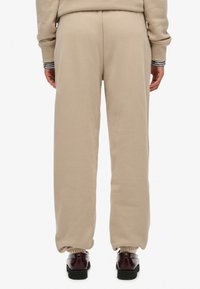 Pantaloni della tuta beige con una vestibilità comoda, dotati di polsini elasticizzati alla caviglia e una texture morbida. Indossati con scarpe scure.