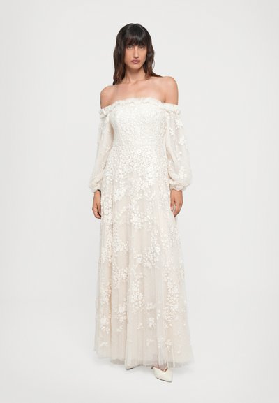 Vestido blanco de tirantes caídos y mangas largas, con embellishments florales y una falda fluida. Tejido suave y texturizado con un velo transparente.