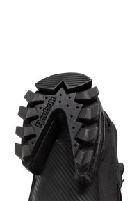 Juodas sportinis batų padas su tekstūruotu guminio sukibimo paviršiumi, su „Reebok“ logotipu ir išskirtiniais daugiakrypčiais protektoriaus raštais.