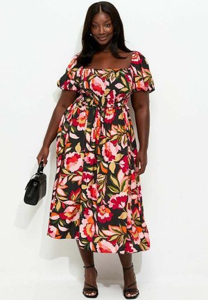 Mujer con vestido midi negro con estampado floral colorido, mangas abullonadas, escote cuadrado, sosteniendo un bolso negro y con zapatos de tacón negros.