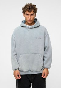 Lichtgrijze oversized hoodie van zachte stof, met een voorzak en geborduurde tekst op de borst. Ribgebreide manchetten en zoom.