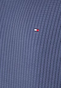 Granatowa prążkowana bawełniana tkanina z małym, wyszywanym logo w kolorach czerwonym, białym i niebieskim po lewej stronie, o teksturowanym wyglądzie.