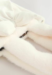 Jucărie moale și pufoasă de culoare albă, cu o fundă mare, netedă, pe partea superioară, având accente negre pe brațe și o căptușeală interioară cu imprimeu de leopard.