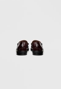 Burgundy patent leather shoes with a low heel, featuring a round toe and silver hardware detail on the back. Smooth texture and slip-on design.