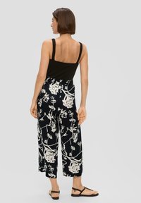 Top sans manches noir associé à un pantalon large à motifs floraux bleu marine avec des designs botaniques blancs, taille élastique et sandales plates noires.