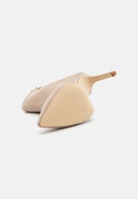 Chaussure à talon aiguille en daim nude avec un bout effilé et une finition lisse. La semelle extérieure est beige avec un motif de grip texturé.