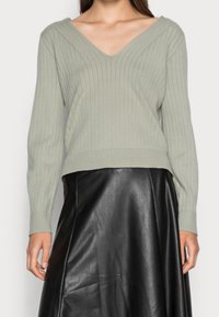 Lichtgroene ribgebreide trui met een V-hals ontwerp, lange mouwen en een cropped zoom, gecombineerd met een zwarte leren rok.