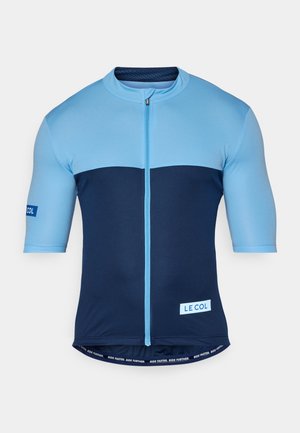 Kratka kolesarska majica s kratkimi rokavi, ki ima svetlo modro zgornji del in temno moder spodnji del, izdelana iz raztegljive tkanine s sprednjim zadrgo in logotipnimi poudarki.