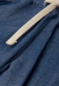 Tela de mezclilla en azul oscuro con una superficie texturizada. Un cordón de color crema pasa por la cinturilla, creando pliegues suaves.