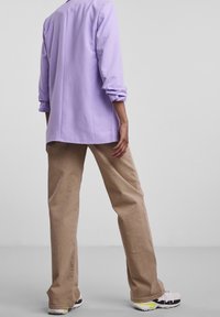 Ljuslila långärmad skjorta med rullade ärmar, tillsammans med beige, löst sittande byxor och vita sneakers med svarta och neonfärgade accenter.