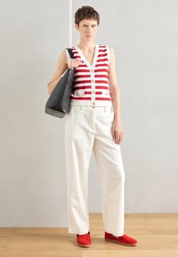 Rood-witte gestreepte mouwloze vest met knoopsluiting, gecombineerd met witte wijde broek en rode schoenen. Zwarte tas accentueert de outfit.
