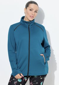 Tyrkysová fleecová bunda s vysokým límcem, černým zipem a akcenty na ramenou; obsahuje kapsy na zip a hladkou texturu.