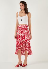 Rood-witte patroon rok met een uitlopende zoom. De rok heeft een asymmetrische snit en bestaat uit een gladde, lichte stof. Gepaard met een witte crop top en rode hakken.