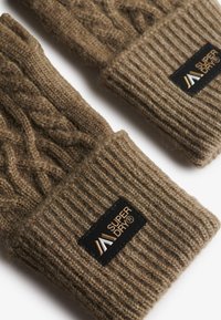 Bruine gebreide handschoenen met geribde manchetten en een kabelbreipatroon, waarbij elke manchette een zwart patch met het "Super Dry" logo heeft.