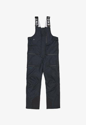 Salopette blu navy con spallacci regolabili, numerose tasche con zip, rinforzi neri sulle ginocchia e una texture del tessuto impermeabile.