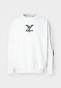 Hvit hettegenser med rund hals, senkede skuldre og lange ermer. Har en svart sommerfugllogotype og tekst på brystet.