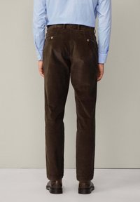 Pantalon en velours côtelé marron avec une coupe droite, doté de poches arrière cousues et de boutons métalliques, porté avec des chaussures sombres.