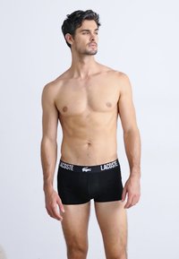 Boxer-briefs noirs avec un logo Lacoste blanc sur la ceinture. Tissu lisse, design ajusté et longueur mi-cuisse.