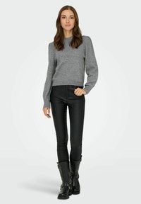 Grauer, gestrickter Pullover mit Puffärmeln, kombiniert mit einer schwarzen, engen Hose und kniehohen schwarzen Stiefeln mit Schnallenakzenten.