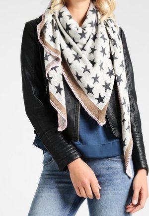 Femme portant un foulard triangulaire à motifs d'étoiles avec une bordure rose sur une veste en cuir noire et une chemise bleue, associée à un jean bleu clair.