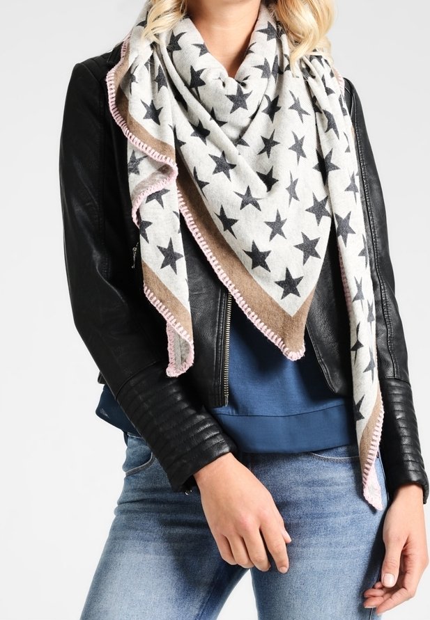 Femme portant un foulard triangulaire à motifs d'étoiles avec une bordure rose sur une veste en cuir noire et une chemise bleue, associée à un jean bleu clair.