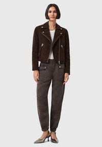 Giacca da motociclista in suede marrone con tasche con zip, abbinata a pantaloni cargo grigi con polsini con coulisse e tacchi metallici a punta.
