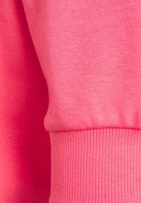Bright pink sweatshirt fabric showcasing a smooth, soft texture with ribbed cuffs. Close-up view emphasizes color and material detail.