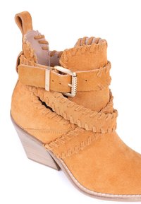 Bottine en daim camel avec un talon empilé, présentant une couture à franges contrastantes et une large bride avec un détail de boucle en or.