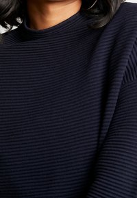 Granatowy Sweter prążkowany z wysokim kołnierzem, z pionowym wzorem i długimi rękawami. Miękki materiał, minimalistyczny design i brak dodatkowych akcentów.