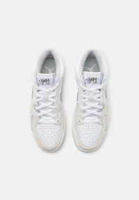 Bílé a světle béžové tenisky s perforovanou špičkou, plochými tkaničkami, z nubukové a kožené materiály, s logem na jazyku a boku.