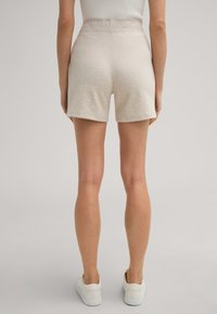 Shorts beige clair avec un motif texturé, taille mi-haute et une ceinture lisse, associés à des baskets blanches.
