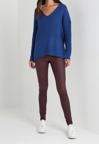 Maglione blu a maglia con scollatura a V e spalle cadenti, abbinato a pantaloni slim-fit bordeaux e scarpe da ginnastica bianche. Tessuto morbido e vestibilità rilassata.