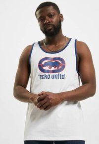 Witte tanktop met blauwe rand, voorzien van een groot rood en blauw logo met een neushoornafbeelding en de tekst "eckō unlt.d." op de voorkant.