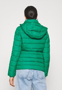Chaqueta de plumas verde con diseño acolchado y capucha. Fabricada con material ligero e aislante. Combinada con jeans de denim claros.
