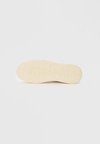 Talpa de sneaker din cauciuc bej, cu un model de profil ondulat, având o textură netedă și margini rotunjite, concepută pentru aderență și confort.