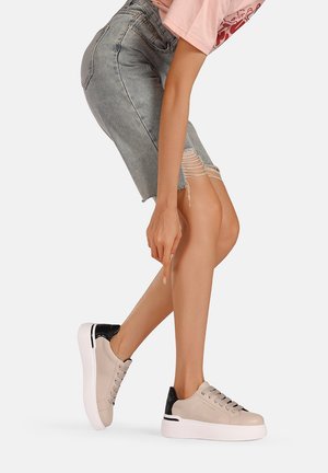 Sneaker in pelle beige con accentazione nera sul tallone, punta rotonda, suola piatta bianca e design con lacci, indossato con una gonna di jeans invecchiata.
