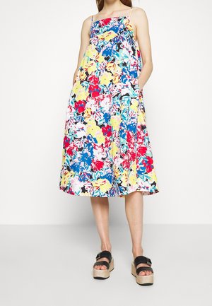 Woman wearing a sleeveless, colorful floral midi dress with thin straps and black platform sandals with buckles.