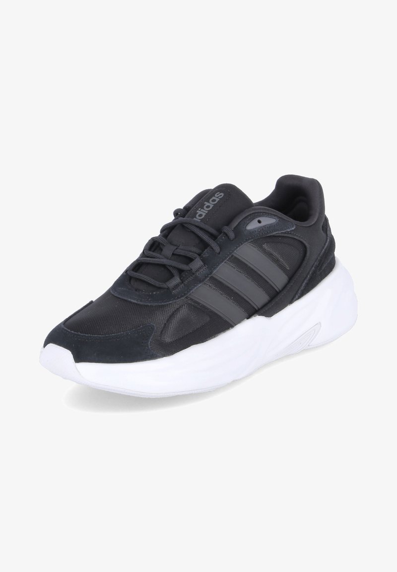 Chaussure de sport noire avec un dessus en mesh et en synthétique, trois rayures grises, un col rembourré et une semelle en caoutchouc blanche.